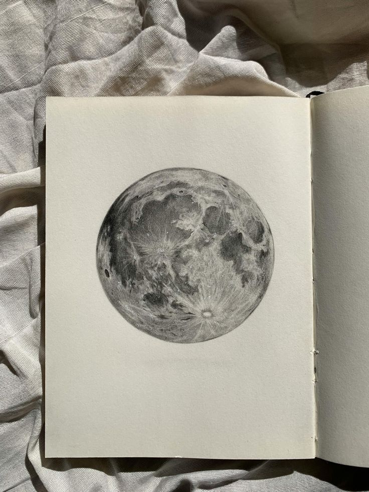 Detailed pencil drawing of the moon on sketchbook paper, illuminated by soft sunlight, creating a serene artistic atmosphere.