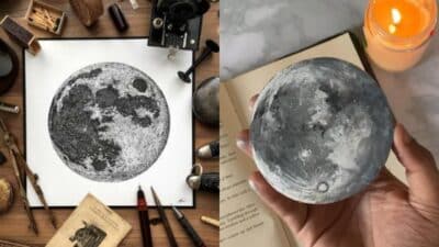 Moon art illustration with vintage tools on a table and a hand holding a realistic moon model, next to an open book and candle.