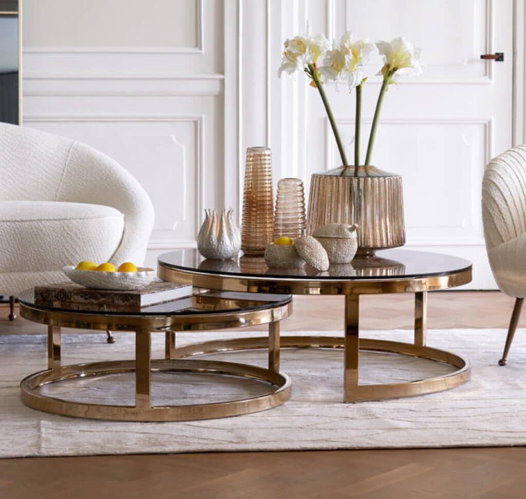 Elegant living room with gold nesting tables, white orchids, and decorative vases. Cozy armchairs add style and comfort to the space.