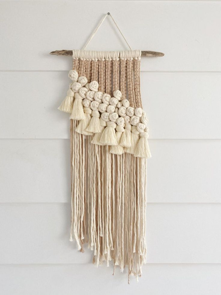 Handmade macramé wall hanging with tassels, featuring cream and beige yarn on driftwood. Boho decor for modern interiors.