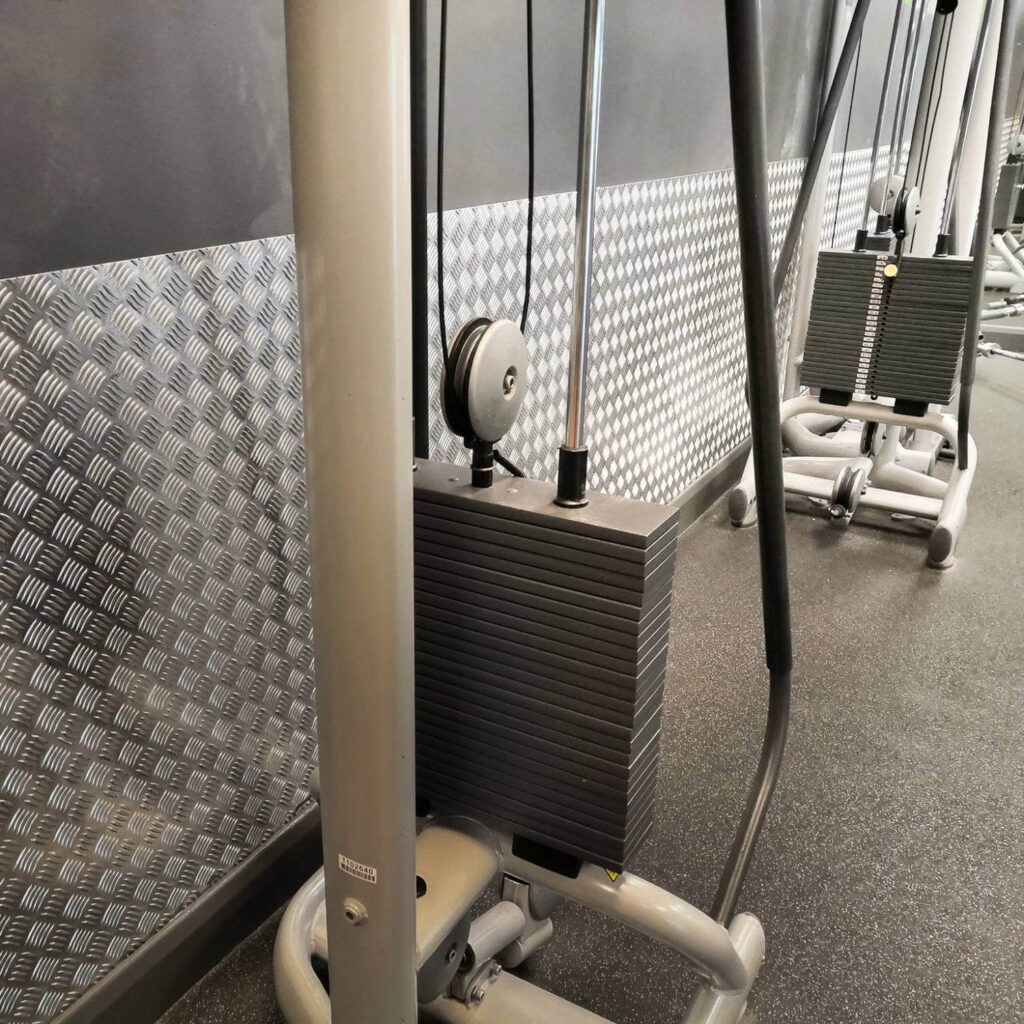 Gym weight stack machine with cables and pulleys in a fitness center.