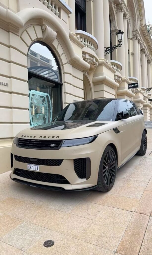 Matte beige Range Rover parked in front of elegant building with decorative columns and arches.