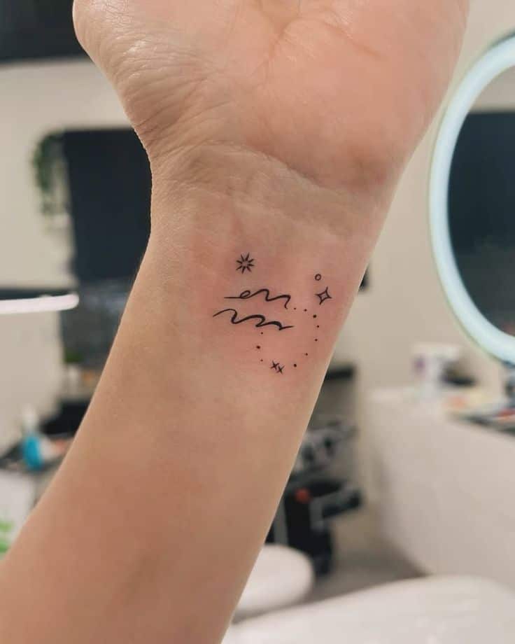 Minimalist tattoo on wrist with abstract cosmic design, including stars and waves, in a modern studio setting.