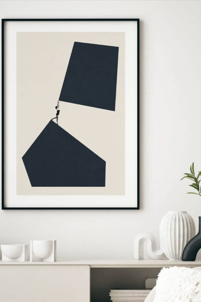 Minimalist grayscale framed artwork of a person lifting geometric shapes against a beige wall background in modern home interior decor.