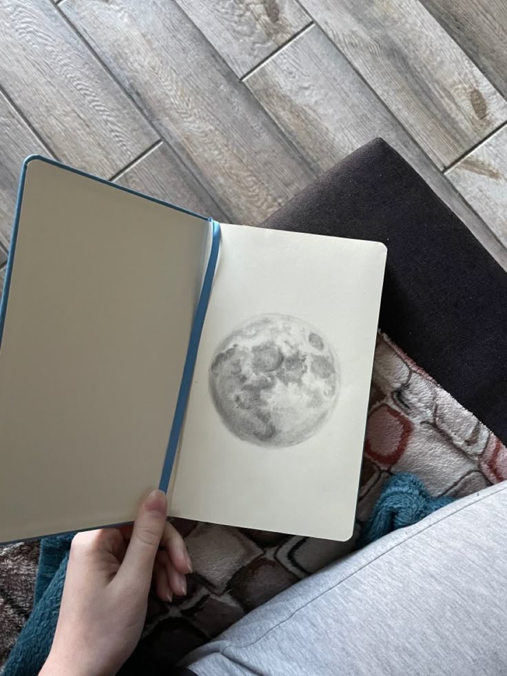 Hand holding a notebook with a detailed moon sketch on a cozy textured background. Perfect for art and astronomy enthusiasts.