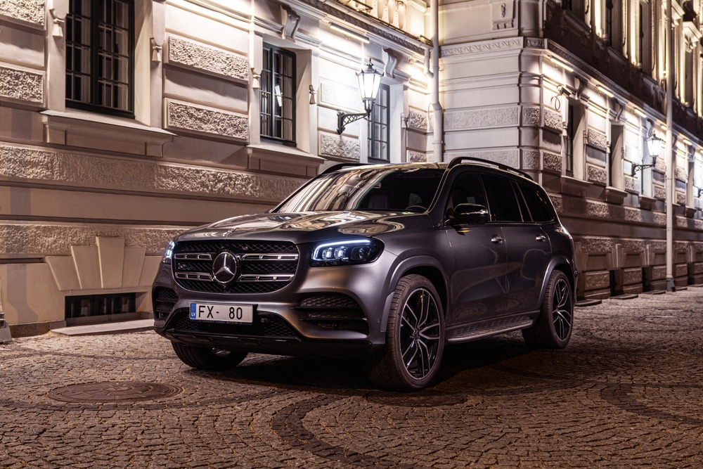 Luxury Mercedes-Benz SUV parked on cobblestone street at night, illuminated by elegant city lights and historic architecture.