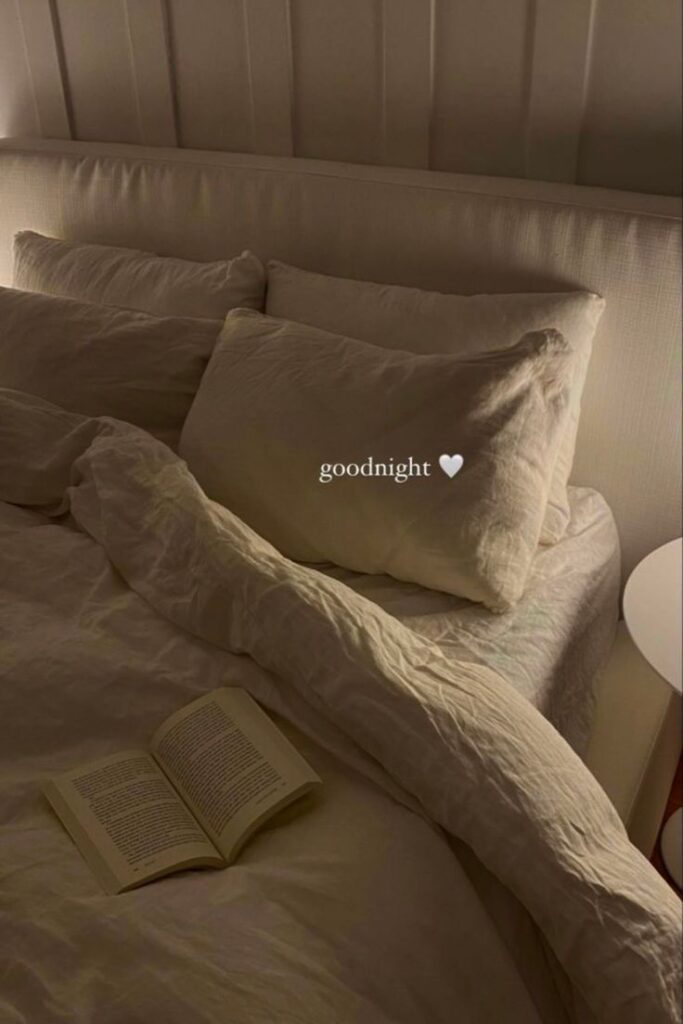 Cozy bed with rumpled sheets, open book, and goodnight text with a heart, creating a warm, relaxing night-time atmosphere.