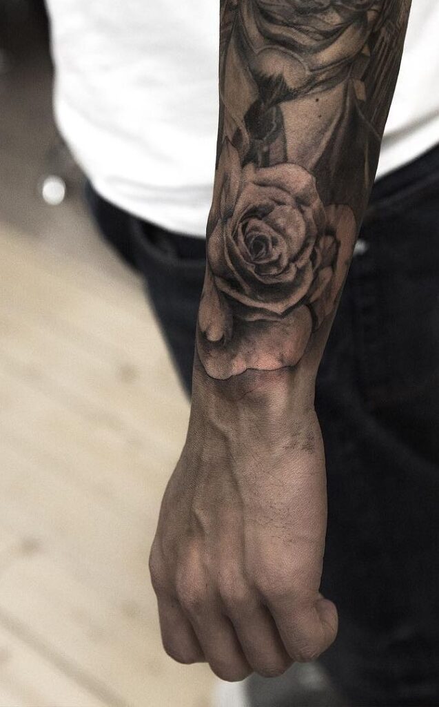 Forearm with detailed black and gray rose tattoo, showcasing intricate floral design artistry and shading on a person's arm.