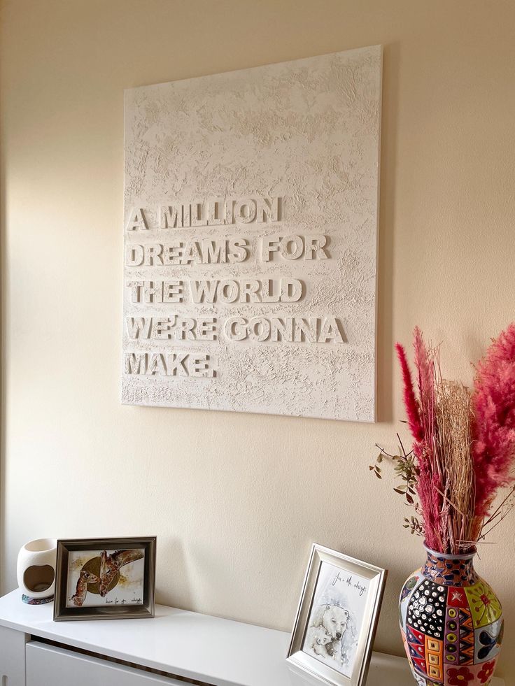 Decorative wall art with inspirational quote above a sideboard, vase of flowers, and framed pictures.