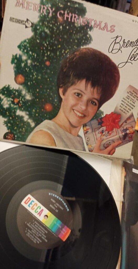 Og Press Brenda Lee Merry Christmas Vinyl Record Album Rockin Around the Christmas Tree Frosty Snowman Strawberry Snow Santa Claus is Comin Vinyl record of Merry Christmas by Brenda Lee with festive cover featuring her smiling by a decorated Christmas tree. | Sky Rye Design Vinyl record of Merry Christmas by Brenda Lee with festive cover featuring her smiling by a decorated Christmas tree.
