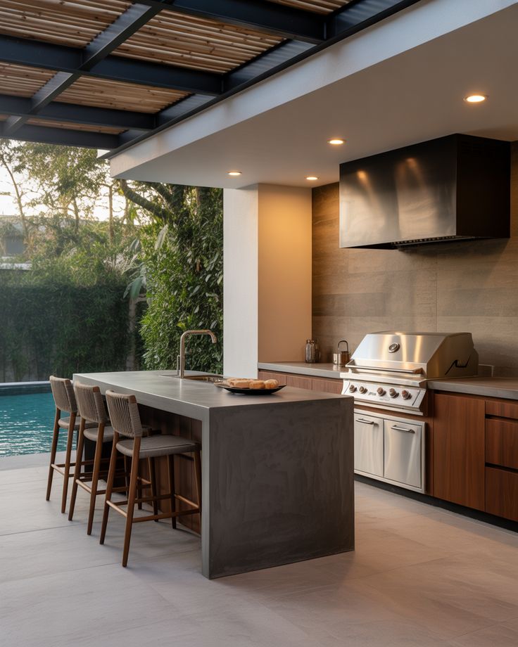 Open Layout Kitchen with Island Modern outdoor kitchen with island, bar stools, grill, and poolside view for a stylish patio dining experience. | Sky Rye Design Modern outdoor kitchen with island, bar stools, grill, and poolside view for a stylish patio dining experience.