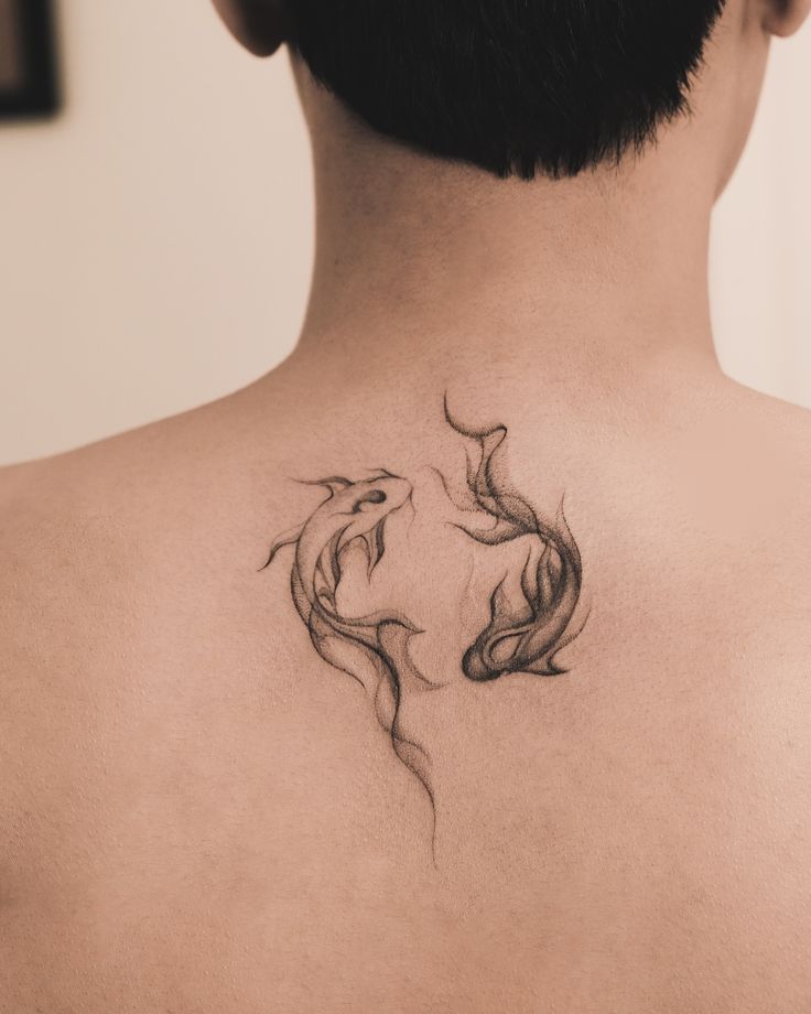Minimalist yin-yang fish tattoo on back, symbolizing balance and harmony. Black ink design with fluid lines on skin.