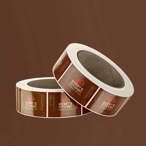 Polypropylene-Synthetic-Labels-Rectangle-Ketchup-Rolljpg Two rolls of custom kitchen labels with a brown design featuring a red apple logo, promoting homemade artisan products on a brown background. | Sky Rye Design Two rolls of custom kitchen labels with a brown design featuring a red apple logo, promoting homemade artisan products on a brown background.
