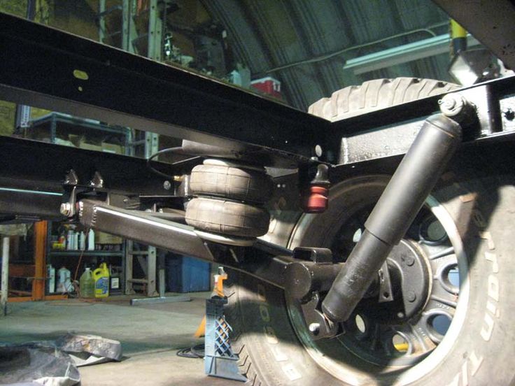 Close-up of vehicle suspension system with shock absorbers and air springs, showcasing automotive engineering details in a workshop.