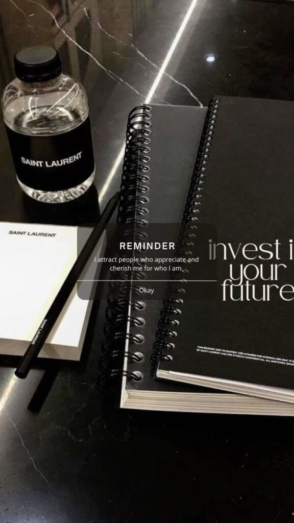 Rich B_tch University Affirmation Wallpaper Phone Lock Screen Saint Laurent notebook, bottled water, and pencil on a sleek black marble surface with motivational reminder text. | Sky Rye Design Saint Laurent notebook, bottled water, and pencil on a sleek black marble surface with motivational reminder text.