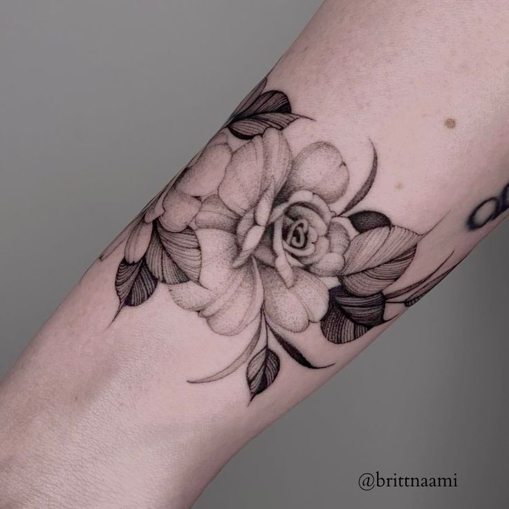 Close-up of a detailed black and gray rose tattoo on a forearm, showcasing intricate shading and delicate petal design.