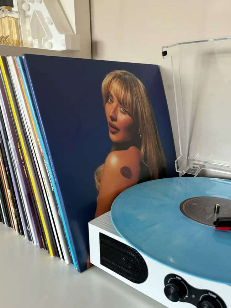 Short and sweet Vinyl record with a blue disc spinning on a turntable, next to an album cover featuring a woman, surrounded by a collection of records. | Sky Rye Design Vinyl record with a blue disc spinning on a turntable, next to an album cover featuring a woman, surrounded by a collection of records.