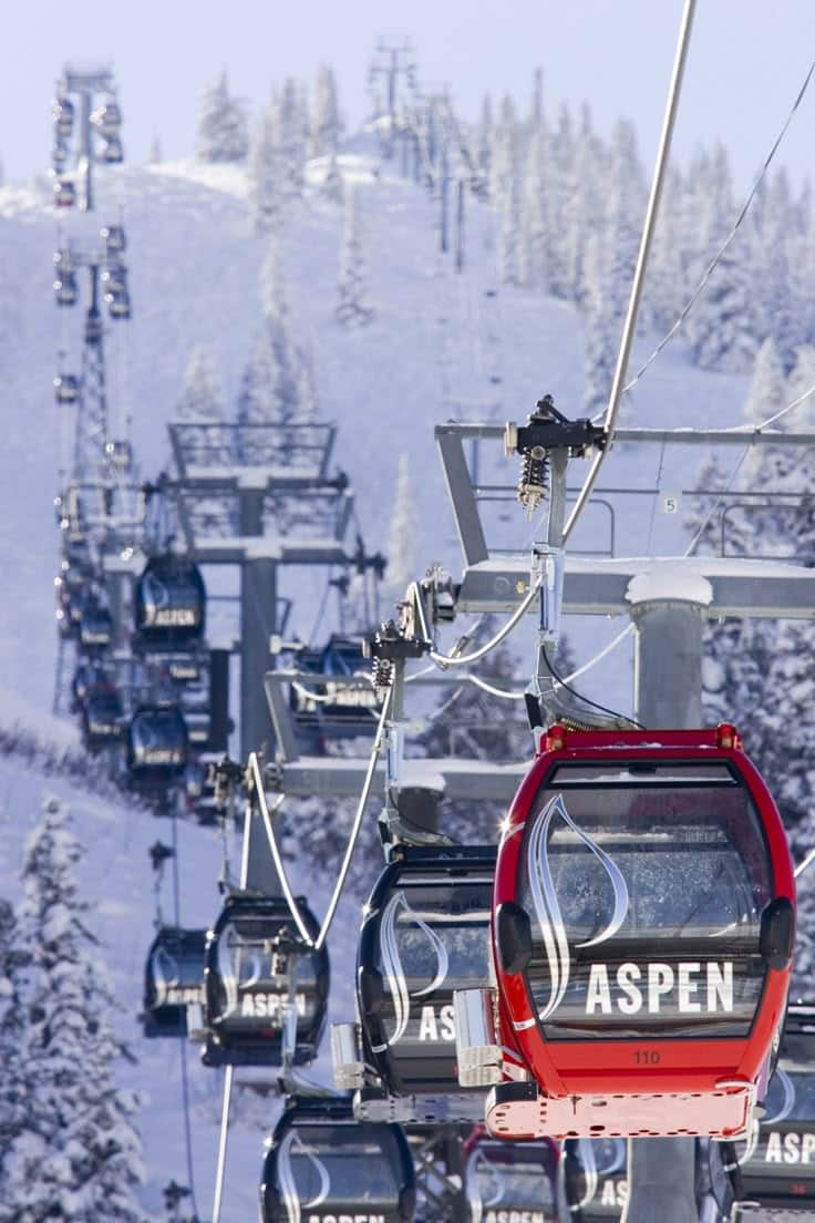 Ski lift gondolas at Aspen Mountain ascending snowy slopes, surrounded by winter trees.
