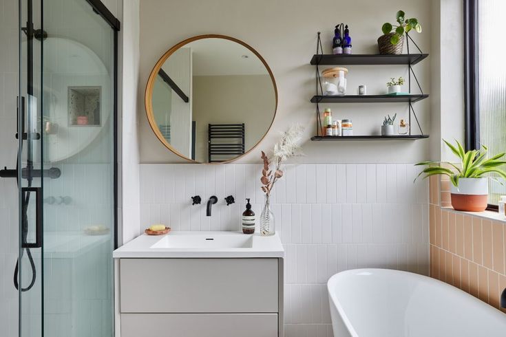 Modern bathroom with round mirror, floating shelves, glass shower, sink, and plants near the window for a fresh look.