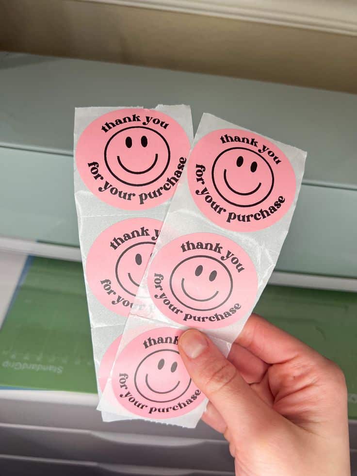 Smiley Face Thank You Small Business Stickers Person holding pink thank you for your purchase stickers with smiley faces, ideal for customer appreciation packaging. | Sky Rye Design Person holding pink thank you for your purchase stickers with smiley faces, ideal for customer appreciation packaging.
