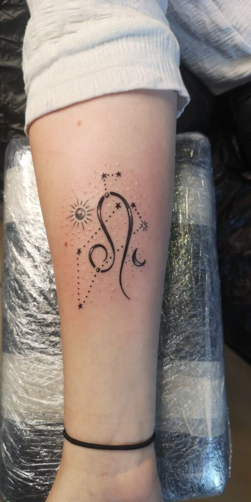 Minimalist zodiac tattoo featuring Leo symbol with stars, sun, and moon on forearm in black ink.