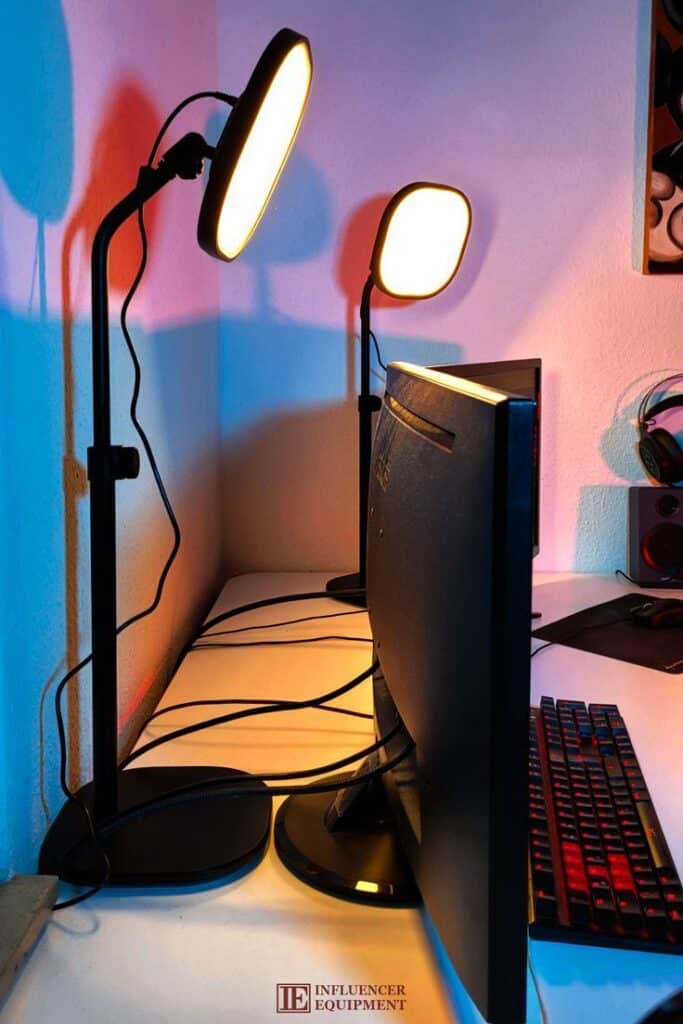 Dual desk lamps illuminate a gaming setup with a monitor and colorful keyboard, creating a vibrant influencer workspace.