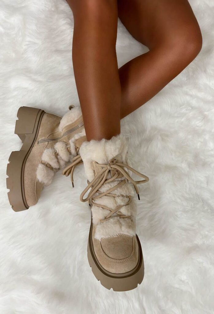 Stylish beige fur-lined winter boots on a fluffy white rug, showcasing cozy fashion for cold weather.