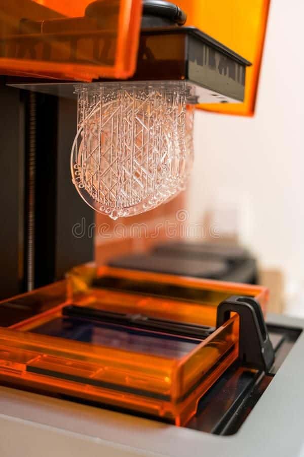 3D printer with orange cover producing intricate clear objects, showcasing advanced additive manufacturing technology.