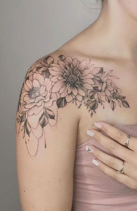 Ornate floral tattoo on woman's shoulder featuring detailed blossoms and leaves, showcasing intricate artistry and elegance.