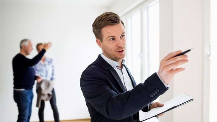 Real estate agent discussing property details with clients in a bright, empty room.