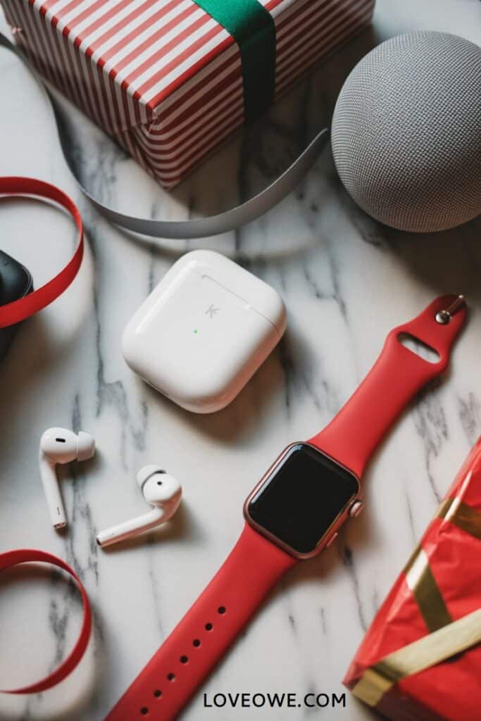 Tech Gadget Christmas Gifts That Work for Everyone Smart watch, wireless earbuds, and a smart speaker next to a striped gift box on a marble surface. | Sky Rye Design Smart watch, wireless earbuds, and a smart speaker next to a striped gift box on a marble surface.