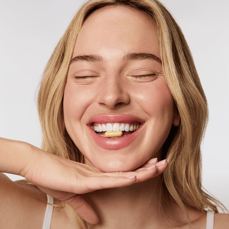 The Gut-Skin Axis + Acne Breakouts _ CLEARSTEM Skincare A joyful woman smiling with a vitamin pill in her teeth, emphasizing wellness and health positivity. | Sky Rye Design A joyful woman smiling with a vitamin pill in her teeth, emphasizing wellness and health positivity.
