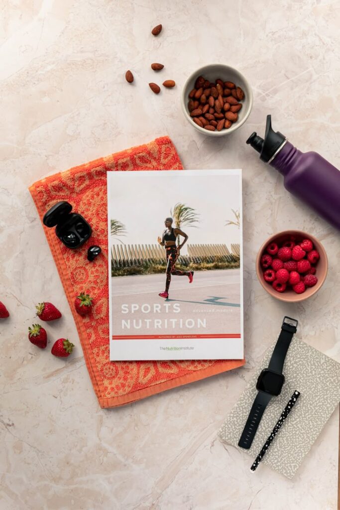 The Nutrition Institute Sports nutrition book with almonds, raspberries, and strawberries on a marble background, alongside a smartwatch. | Sky Rye Design Sports nutrition book with almonds, raspberries, and strawberries on a marble background, alongside a smartwatch.