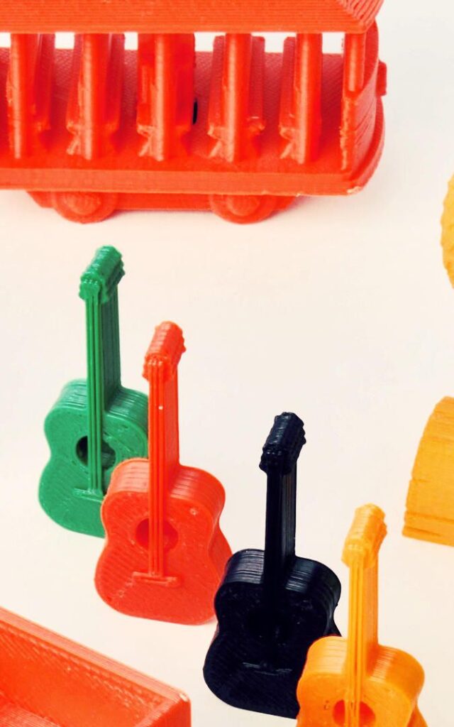 Colorful 3D printed models: red trolley, green, orange, and black guitars on white background, showcasing creative design.