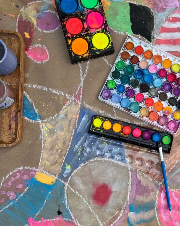 Colorful watercolor palettes and paintbrush on an abstract painted table, showcasing vibrant artistic creativity and expression.