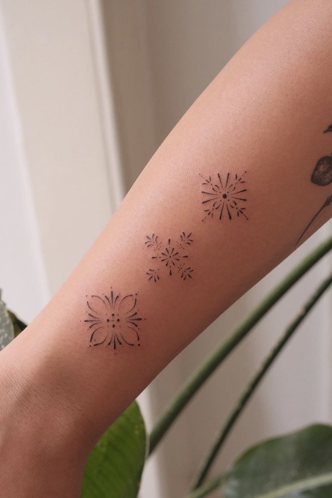 Minimalist floral and geometric tattoos on forearm, showcasing intricate black ink designs against skin.