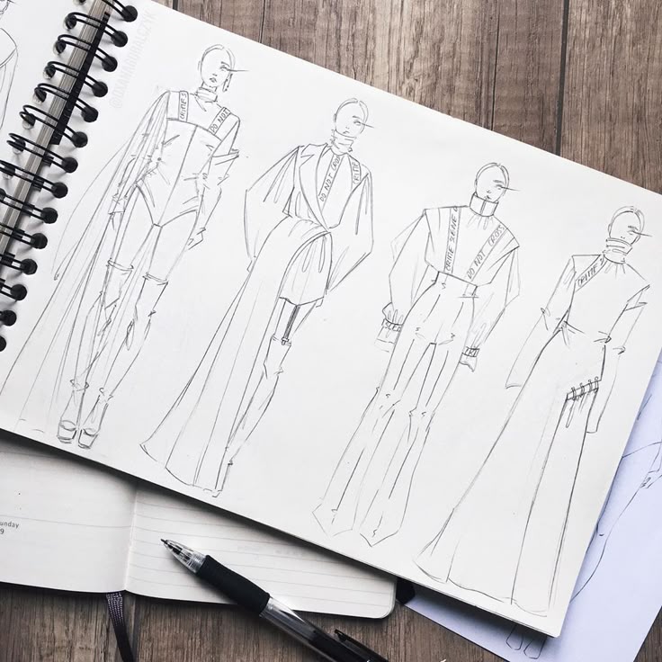 Fashion sketches of four stylish outfits in a sketchbook with a pen on a wooden table. Perfect for design inspiration and creativity.