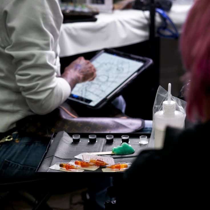 Tattoo artist working on a design with a digital tablet, surrounded by tattoo ink and equipment on a tray.