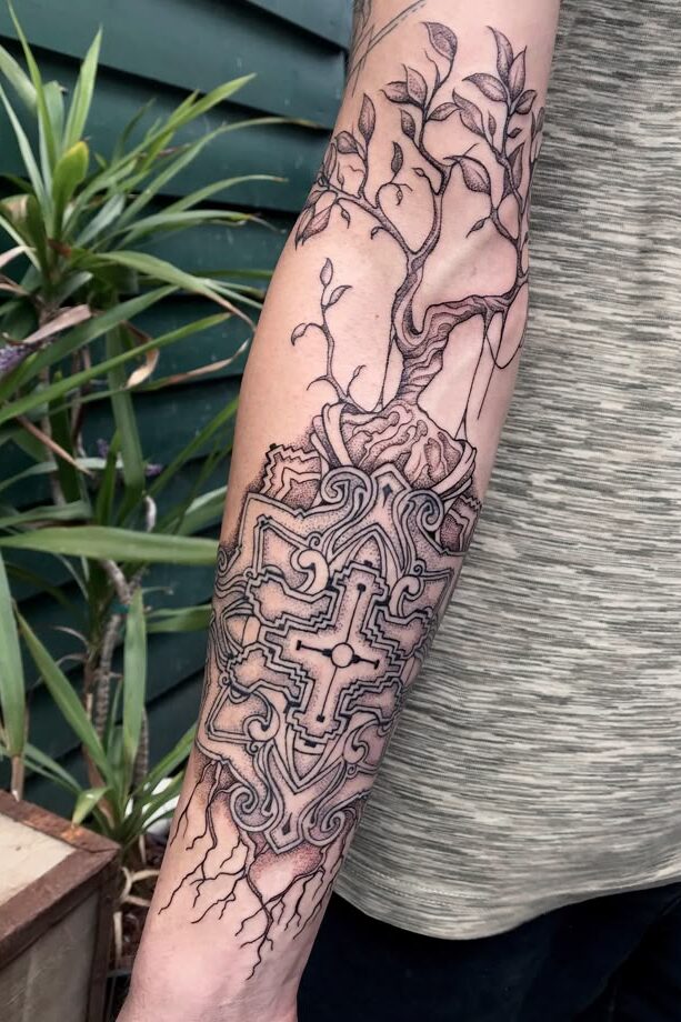 Abstract tree and cross tattoo on forearm with intricate details.