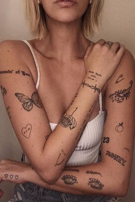 Trending Ideas _ Arm Tattoos For Women Woman with diverse tattoos on arms, featuring butterflies, barbed wire, hearts, and more, wearing a white tank top. | Sky Rye Design Woman with diverse tattoos on arms, featuring butterflies, barbed wire, hearts, and more, wearing a white tank top.