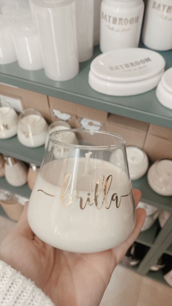 Vela palabra dorada Hand holding a decorative candle with brilla text, surrounded by white bathroom accessories on a shelf. Cozy, minimalist decor. | Sky Rye Design Hand holding a decorative candle with brilla text, surrounded by white bathroom accessories on a shelf. Cozy, minimalist decor.