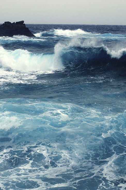 Very Strong Rich Blue Ocean waves crashing against rocks under a cloudy sky, depicting the power and beauty of nature's seascape. | Sky Rye Design Ocean waves crashing against rocks under a cloudy sky, depicting the power and beauty of nature's seascape.