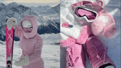 A person in a pink ski outfit holding skis on a snowy mountain with goggles and gloves.