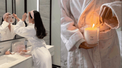 Woman enjoying self-care routine with face mask in bathroom, lighting a scented candle while wearing a cozy robe for relaxation.