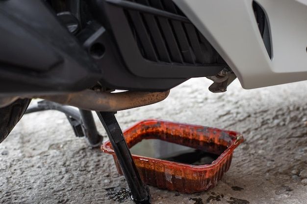 Motorcycle undergoing oil change with a red pan collecting used oil, highlighting routine maintenance on a concrete surface.