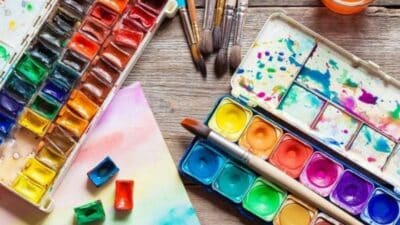 Colorful watercolor paint palettes with brushes and paper on a wooden table, perfect for creative art projects and painting inspiration.
