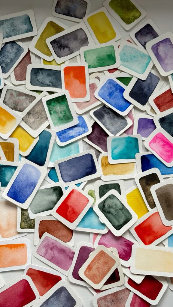 Scattered watercolor swatches in various vibrant hues on white paper, showcasing a colorful palette for artistic inspiration and creativity.