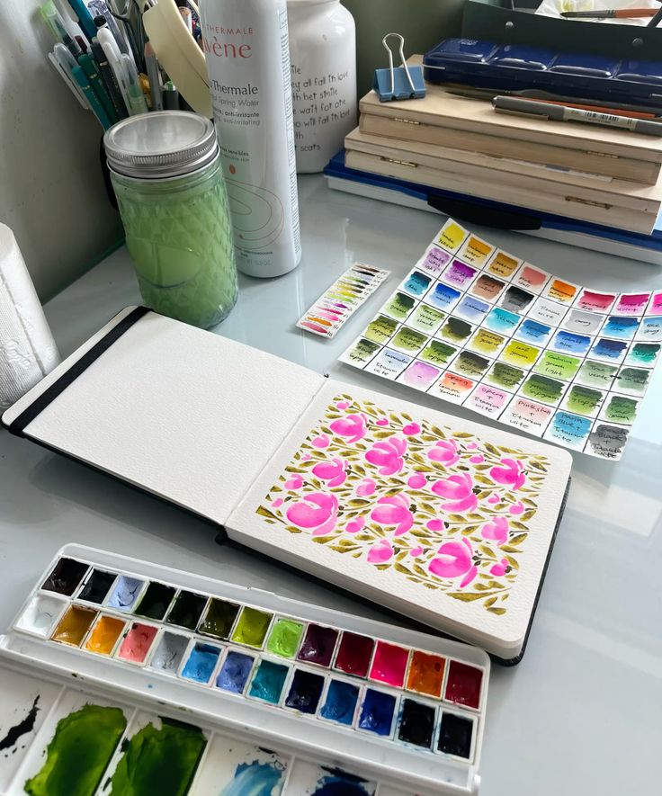 Watercolor switch Art studio with watercolor paints and open sketchbook showing pink floral design. Color swatches and art supplies in the background. | Sky Rye Design Art studio with watercolor paints and open sketchbook showing pink floral design. Color swatches and art supplies in the background.