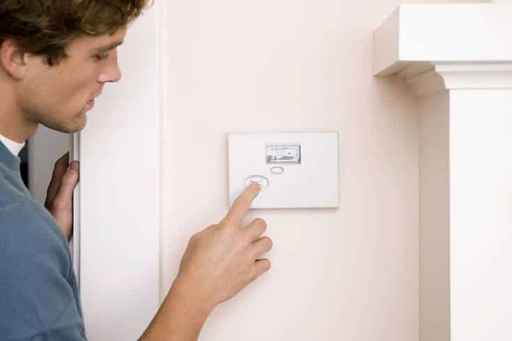 Man adjusting home thermostat on wall, optimizing energy usage for comfort.