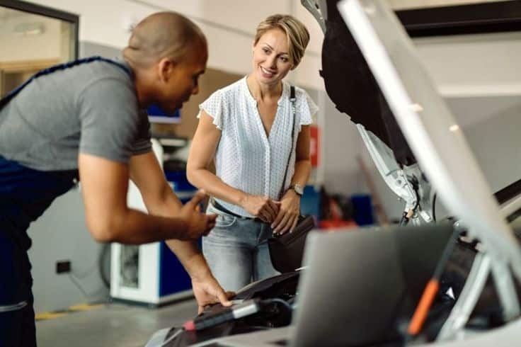 When Do You Need to Call a Car Mechanic_ Mechanic explaining car repair to a smiling customer at an auto shop. | Sky Rye Design Mechanic explaining car repair to a smiling customer at an auto shop.
